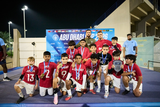 Youth football team celebrating victory at the Abu Dhabi Cup 2026 with medals and a trophy on stage.