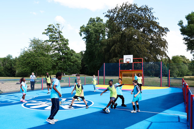 Children playing soccer on a colorful outdoor court with basketball hoops.