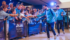 A group of people wearing Manchester City attire interact with players in a setting marked by 'Asahi Tunnel Club' signage.