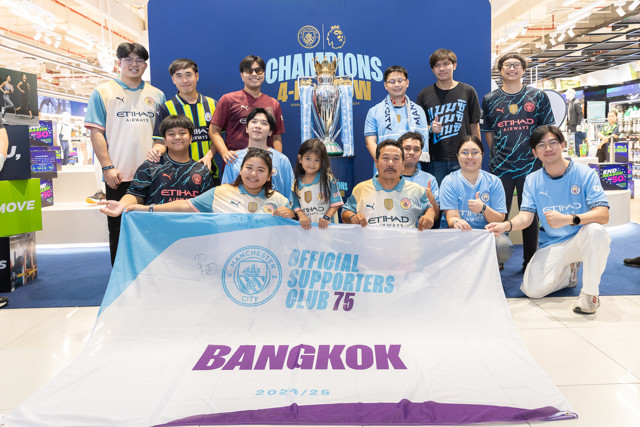 Group of Manchester City fans in official club gear, posing with Premier League trophy. They hold a banner that reads 'Official Supporters Club 75 Bangkok 2024/25'.