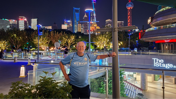 Person in a Manchester City jersey posing in a cityscape setting with illuminated skyscrapers and urban lights at night.