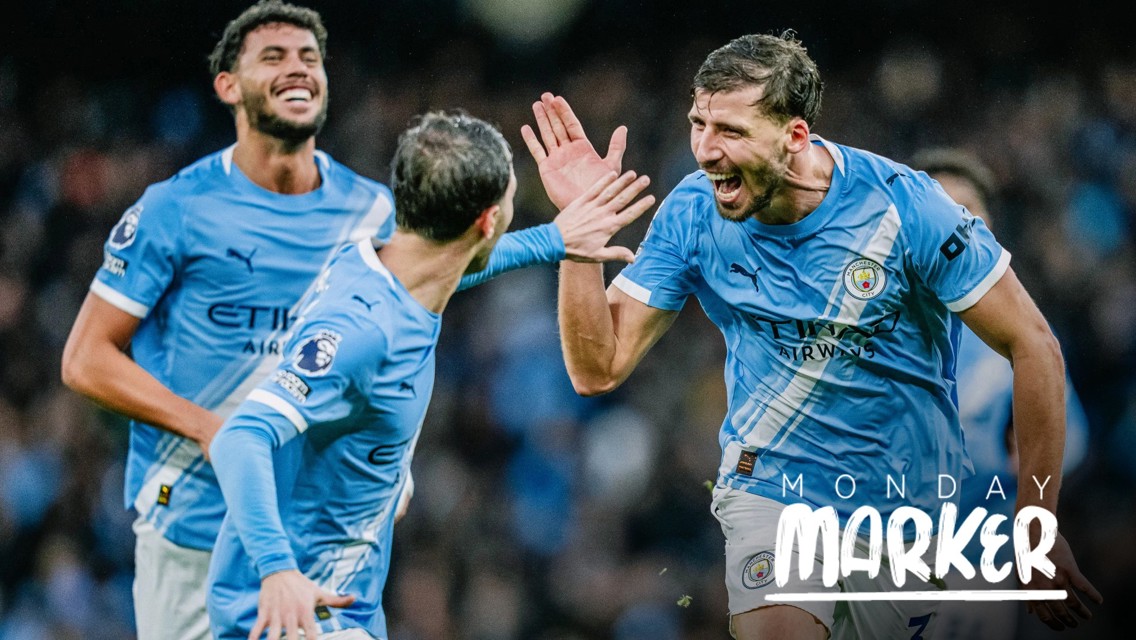 Three Manchester City players in blue jerseys celebrate a goal, high-fiving. The image has the text 'Monday Marker' on it.