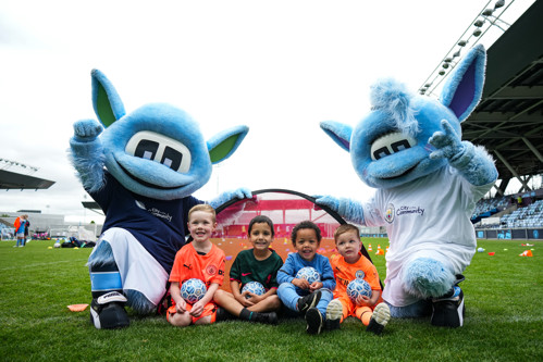 Manchester City's mascots posing for a picture with City in the Community participants on a football pitch.
