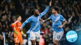 Two Manchester City players in light blue kits celebrating a goal with a high five, while a goalkeeper in an orange kit stands in the background.
