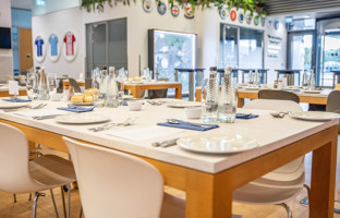 Restaurant setting with neatly arranged tables, cutlery, and water bottles, decorated with football jerseys and logos on walls.