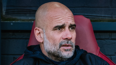 A person with their face blurred is seated in a red sports chair, wearing a dark jacket.