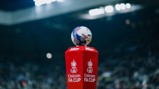 A Mitre ball is placed on a red stand marked with 'Emirates FA Cup' at a football stadium.