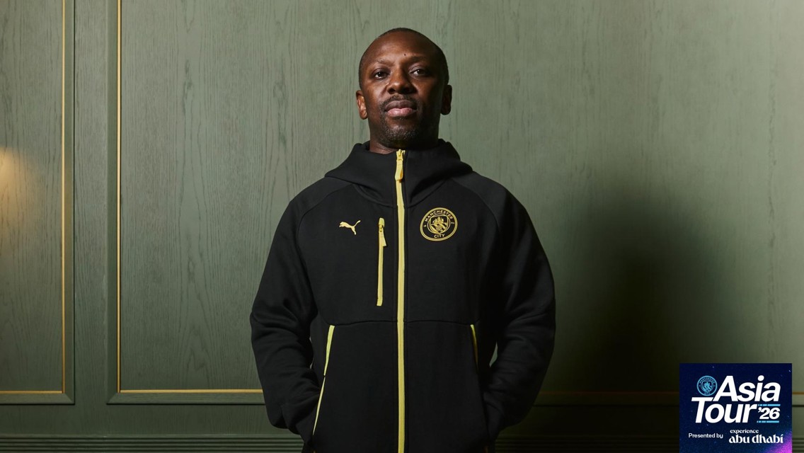 A person in a Manchester City hoodie. The backdrop features 'Asia Tour 26' presented by Experience Abu Dhabi in the corner.