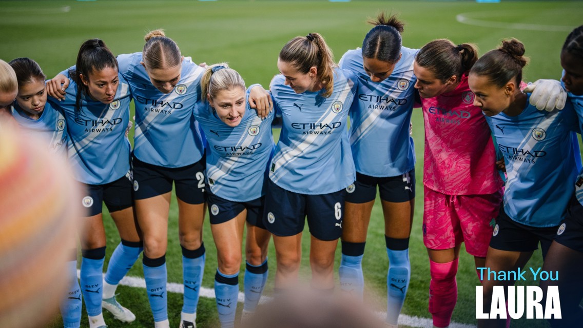 A group of Manchester City women players huddling on a soccer field wearing blue jerseys. Text says 'Thank You Laura.'