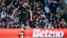 A Manchester City player in black kit with Etihad Airways branding dribbles the ball on the field during a match.