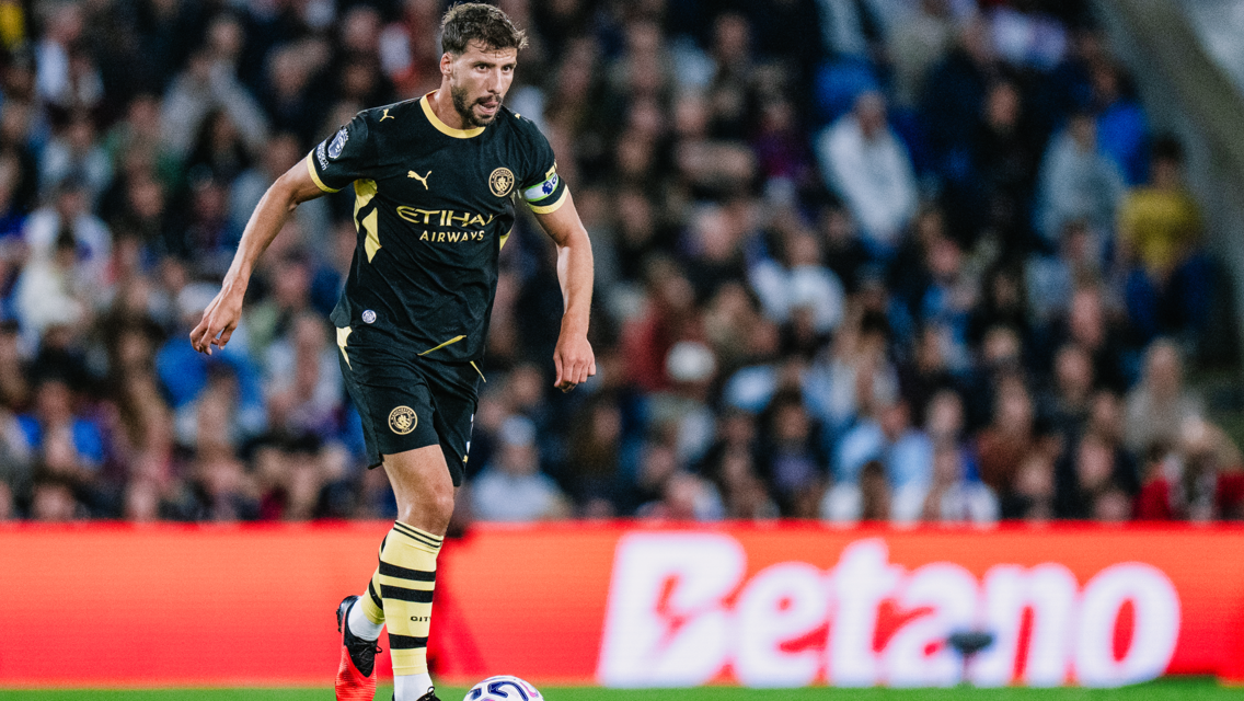 A Manchester City player in black kit with Etihad Airways branding dribbles the ball on the field during a match.