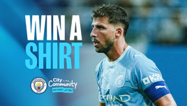 A Manchester City player wearing a blue kit is featured with text 'Win a Shirt' and Manchester City and City in the Community logos.