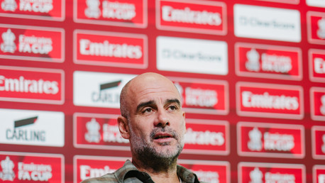 A press conference setting with a blurred face in front of a backdrop featuring 'Emirates FA Cup' logos.