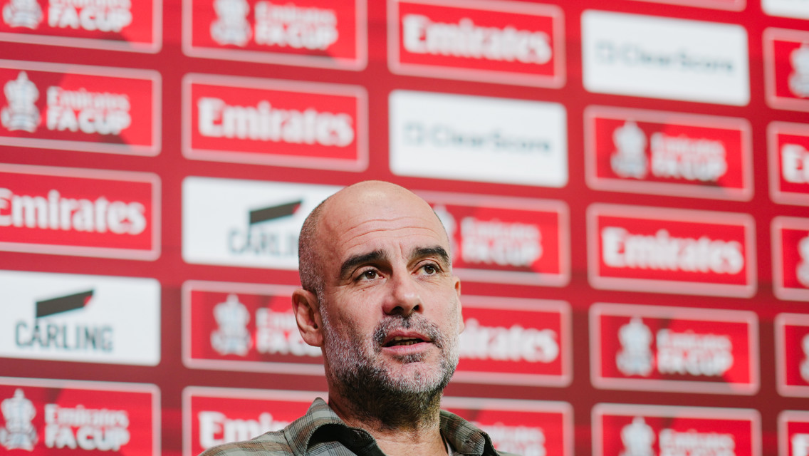 A press conference setting with a blurred face in front of a backdrop featuring 'Emirates FA Cup' logos.