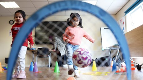 Children participating in a play activity with a football inside a room with cones and rings.