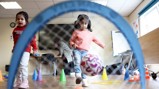 Children participating in a play activity with a football inside a room with cones and rings.