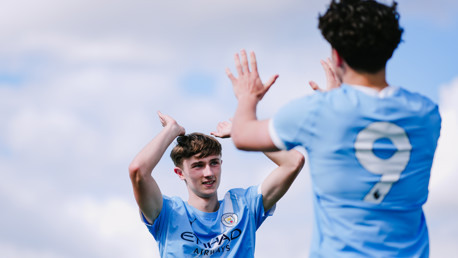 Two soccer players in blue jerseys are celebrating with high-fives. The jersey has the Manchester City emblem and 'Etihad Airways' logo.