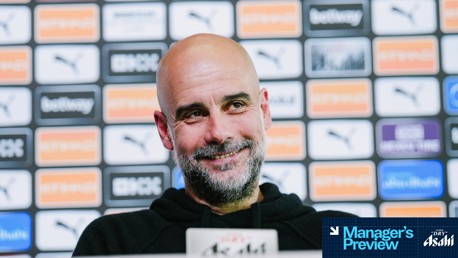 Blurred face of a person speaking at a press conference with a background featuring sponsorship logos including Puma and Etihad.