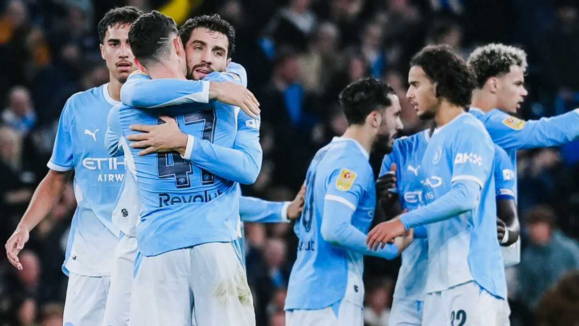 A group of Manchester City players in light blue kits, celebrating on a football field.