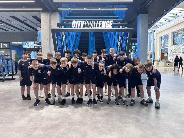 A group of young people in matching sports attire pose together in a retail space with a 'City Challenge' sign above. The environment is modern with displays of sports gear.