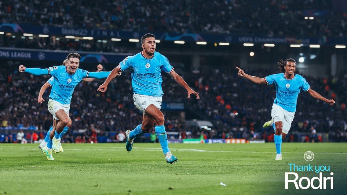 Players in Manchester City jerseys celebrating a goal on the soccer field during a UEFA Champions League match. Text reads 'Thank you Rodri'.