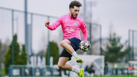 Soccer player in a pink Manchester City training kit controls a ball on a field.