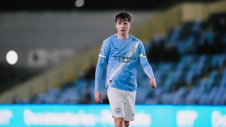 A Manchester City player wearing the team's light blue home kit with Etihad Airways as the sponsor on the jersey, walking on the field with blurred face.