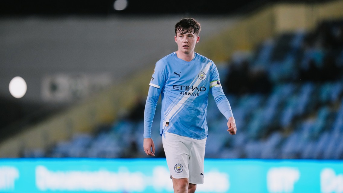 A Manchester City player wearing the team's light blue home kit with Etihad Airways as the sponsor on the jersey, walking on the field with blurred face.