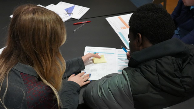 A woman and a man working together on a document at a table. The woman is pointing at a part of the document.