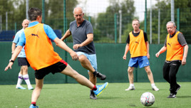 Men playing soccer on a field; some are wearing orange training bibs.