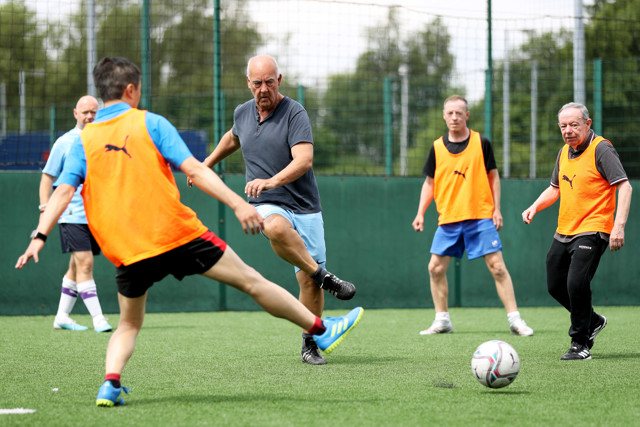 Men playing soccer on a field; some are wearing orange training bibs.