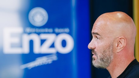 A bald man with a beard is in profile, facing a blue background with text reading 'Enzo'.