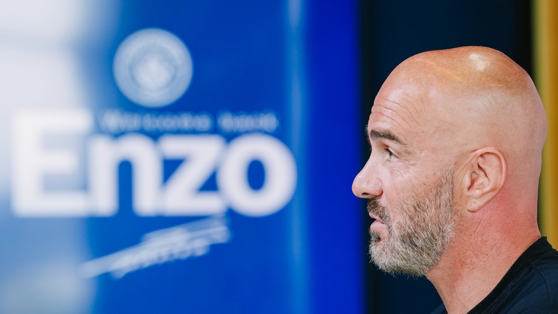 A bald man with a beard is in profile, facing a blue background with text reading 'Enzo'.