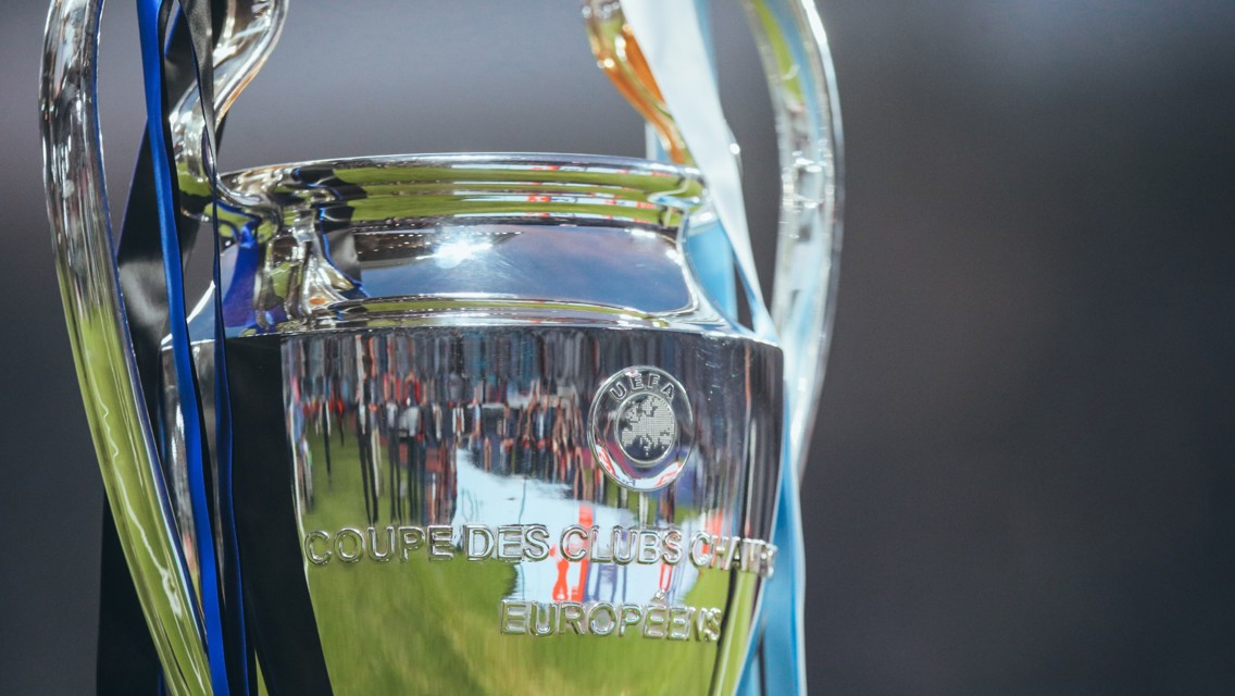 Close-up of the UEFA Champions League trophy with reflections on the surface and blue and black ribbons attached.
