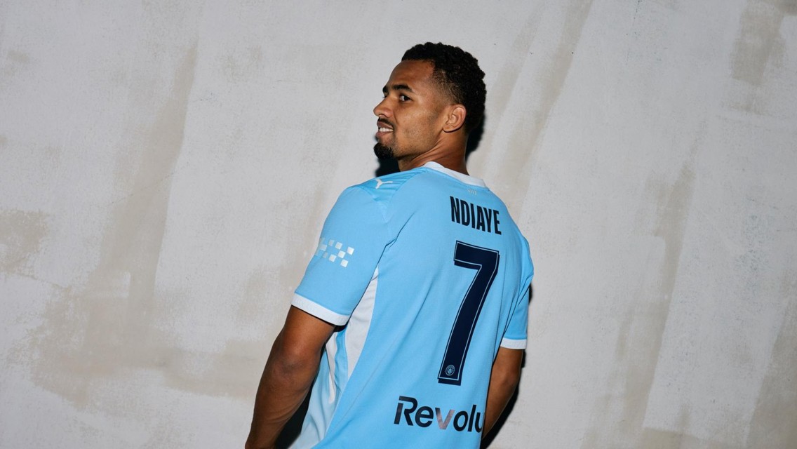 A soccer player wearing a light blue jersey with the name 'NDIAYE' and number 7 on the back looks over his shoulder.