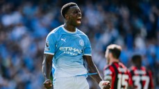 A football player wearing a Manchester City jersey celebrates on the field during a match. The jersey features the Etihad Airways logo and Premier League patch.