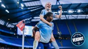 Two women's soccer players in Manchester City uniforms celebrate a goal at a stadium.