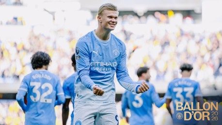 A soccer player in a Manchester City jersey celebrates on the field. Teammates surround him with the 'Ballon D'Or 2026' text overlay.