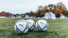 Three Puma footballs on a grassy training pitch.
