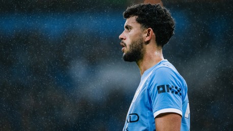 Side view of a Manchester City player wearing a blue jersey during a rainy match with a blurred face.