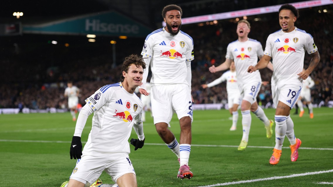 Leeds United soccer players celebrating on the field in full kit with visible sponsored Red Bull logo and Leeds United crest.