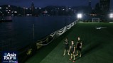 Three players in Manchester City jerseys stand on an illuminated football pitch next to a waterfront in Hong Kong as part of the Asia Tour '26.