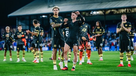 Manchester City players in black kit celebrating on the field with clapping and cheering after a match.