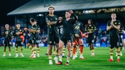 Manchester City players in black kit celebrating on the field with clapping and cheering after a match.