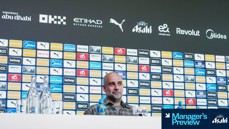 Press conference setup with branded backdrop and table items, including bottled drinks and a table sign showing Manager's Preview at Etihad Stadium.