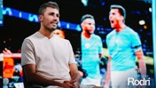 A person sitting and talking in front of a background showing two other people in Manchester City jerseys with the text 'Thank you Rodri' at the bottom.
