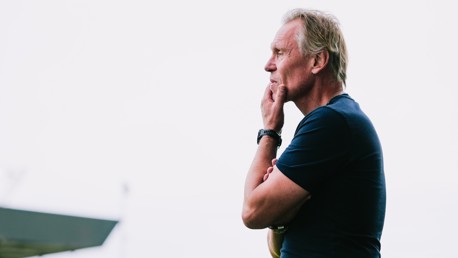 A man standing sideways, thoughtfully touching his chin with a watch on his wrist.