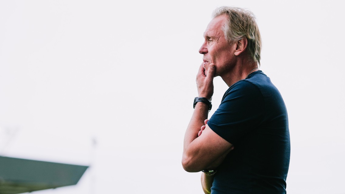 A man standing sideways, thoughtfully touching his chin with a watch on his wrist.