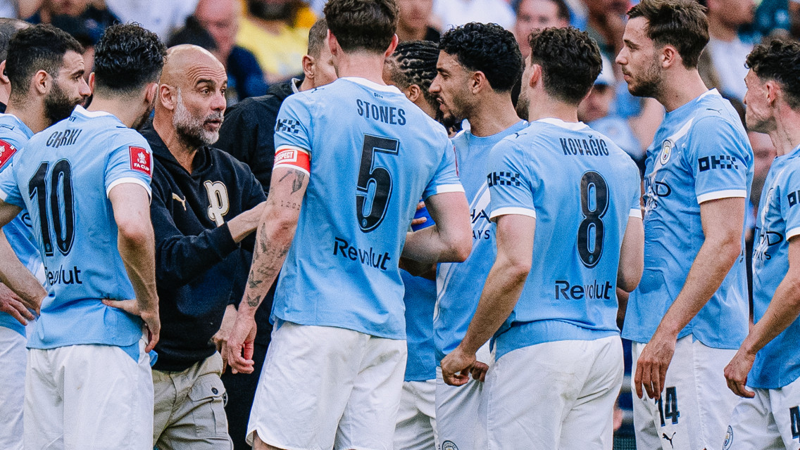 A group of Manchester City players wearing blue jerseys with visible names and numbers engaged in discussion during a match.