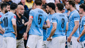 A group of Manchester City players wearing blue jerseys with visible names and numbers engaged in discussion during a match.